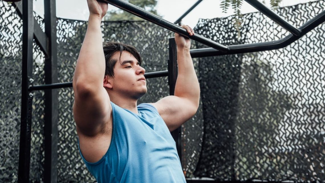 Muscular man in blue tank top performing pull-ups outdoors in Mexico City.
